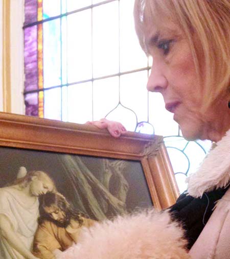 Photo by Nick Fiala Pastor Jill Walker examines one of the original paintings left behind when the structure was built as the Catholic Church in Lovington which remained open from 1915 until the late 1980s.