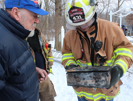 Photo by RR Best Fire Destroys Rural Sullivan Home Findlay fire chief Ed Voltenburg presents burned strong box to Jim Binion following a blaze that totally destroyed his home on 850 E County Road outside Sullivan. Windsor, Bethany and Sullivan fire departments joined to fight the 12:16 p.m. January 20 fire. Sullivan Fire Department reports indicated the Binions saw flames in the center of the house and were able to escape to their daughter’s home next door. They watched the family home destroyed by fire while sitting at son-in-law and Findlay fire chief Voltenburg’s home. Red Cross also lent assistance at the fire scene. Firefighters remained at the Binion home using a backhoe to help expose hot spots until 4 p.m.